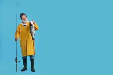 Photo of Fisherman with rod and catch on light blue background, space for text