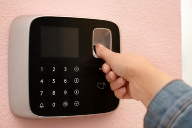 Photo of Woman scanning fingerprint on alarm system, closeup