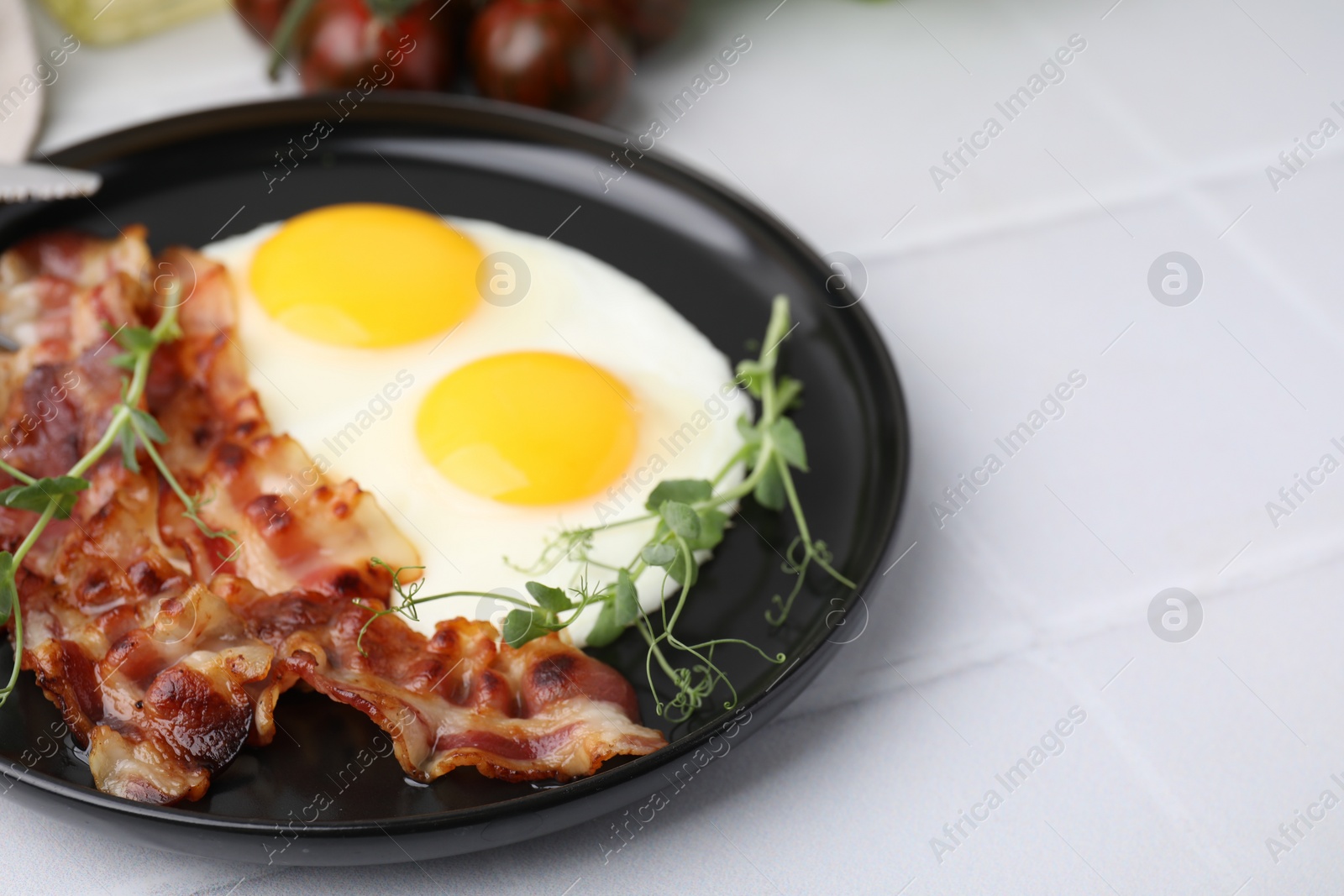 Photo of Fried eggs, bacon and microgreens on white tiled table, closeup. Space for text