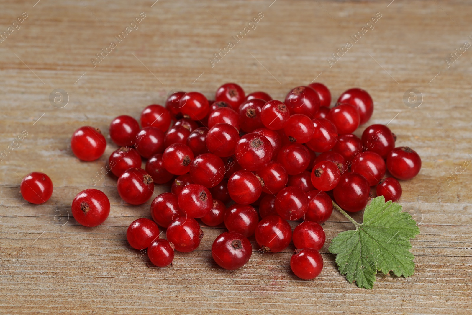 Photo of Pile of ripe red currants and leaf on wooden table, closeup