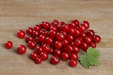 Photo of Pile of ripe red currants and leaf on wooden table, closeup