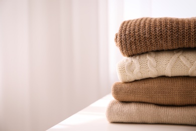 Stack of folded warm sweaters on white table indoors, closeup. Space for text