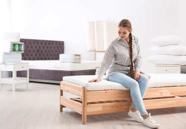 Photo of Young woman testing mattress in furniture store. Space for text