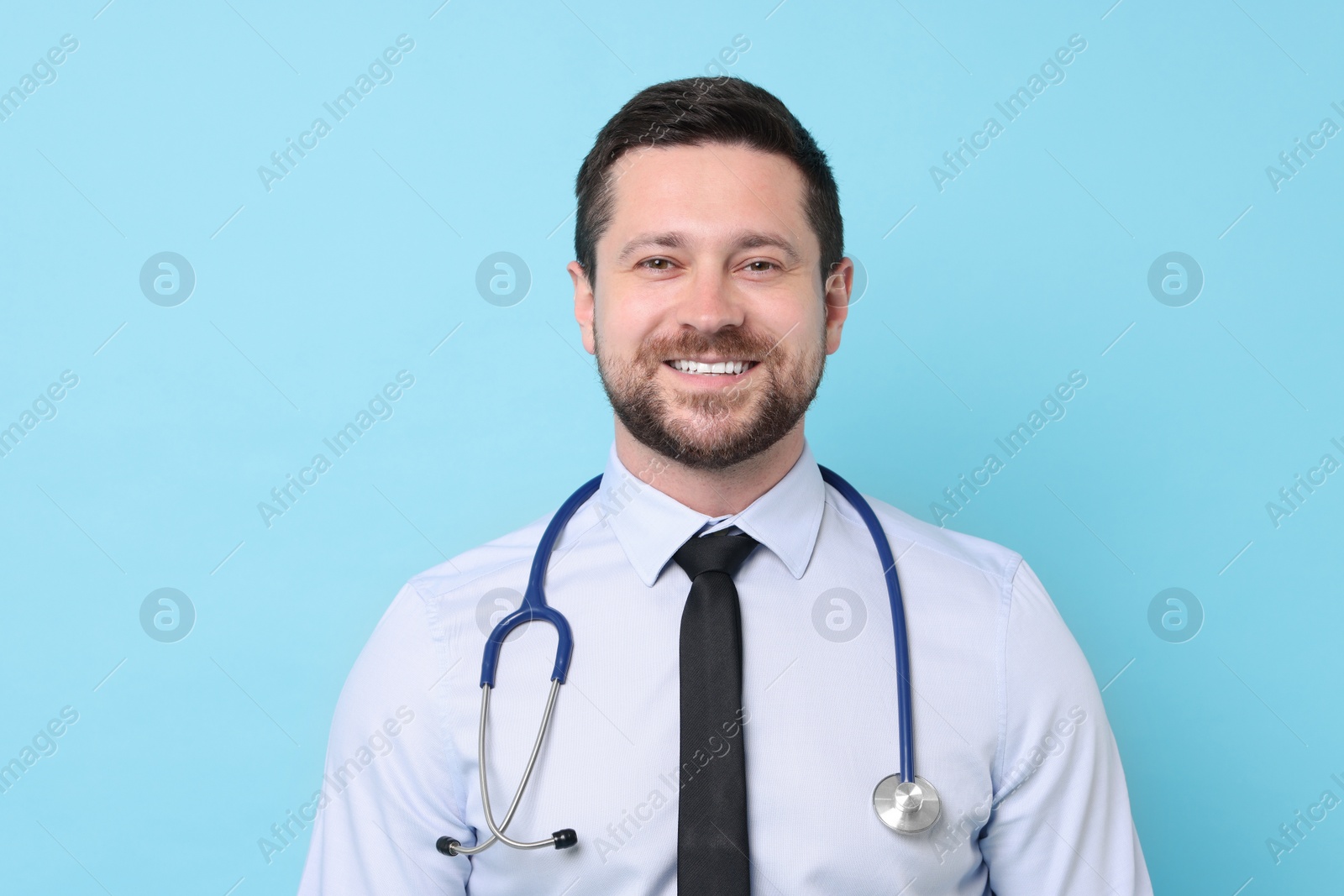 Photo of Smiling doctor with stethoscope on light blue background