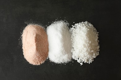 Different types of organic salt on black table, top view