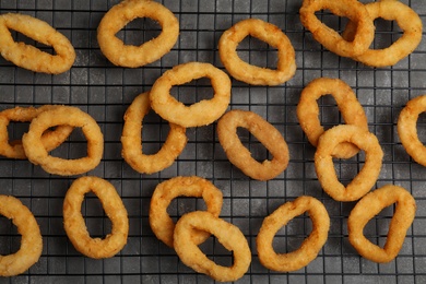 Photo of Cooling rack with fried onion rings on grey table, top view