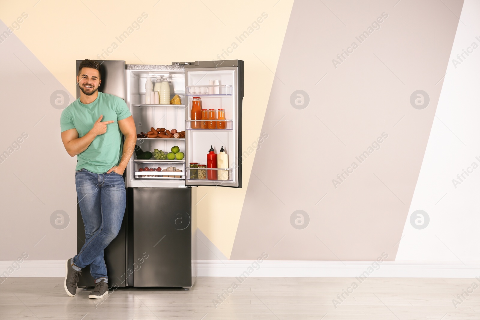 Photo of Happy young man near open refrigerator indoors, space for text