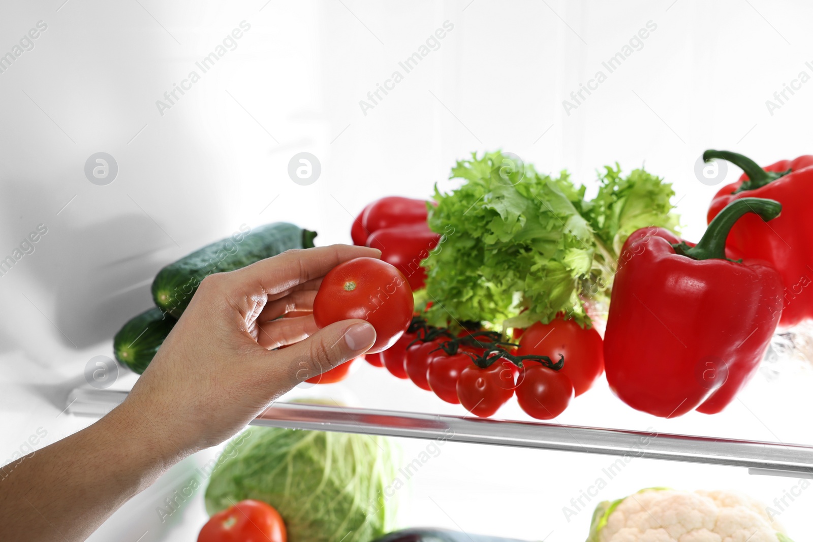 Photo of Young woman taking tomato out of refrigerator, closeup