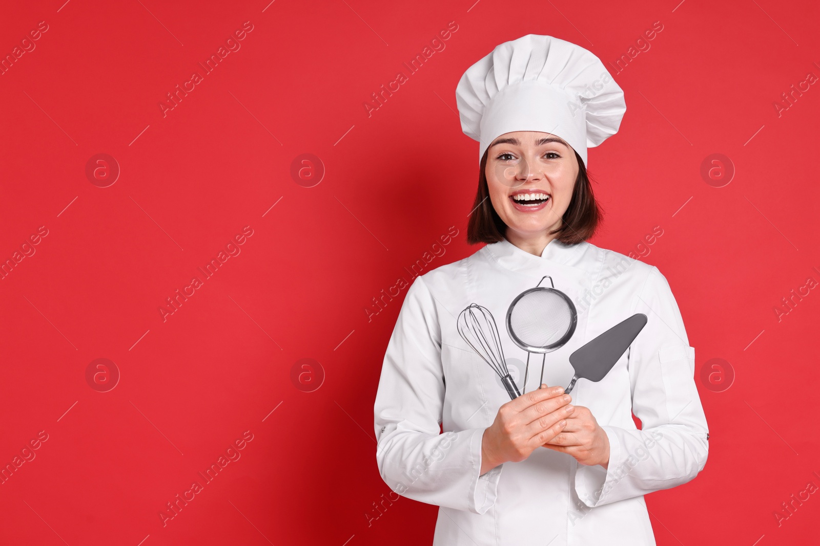 Photo of Happy confectioner holding professional tools on red background, space for text