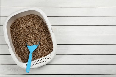 Photo of Cat litter tray with filler and scoop on white wooden floor, top view. Space for text