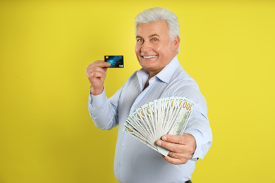 Happy senior man with cash money and credit card on yellow background