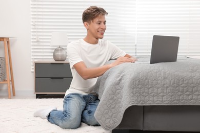 Photo of Happy young man having video chat via laptop on bed indoors