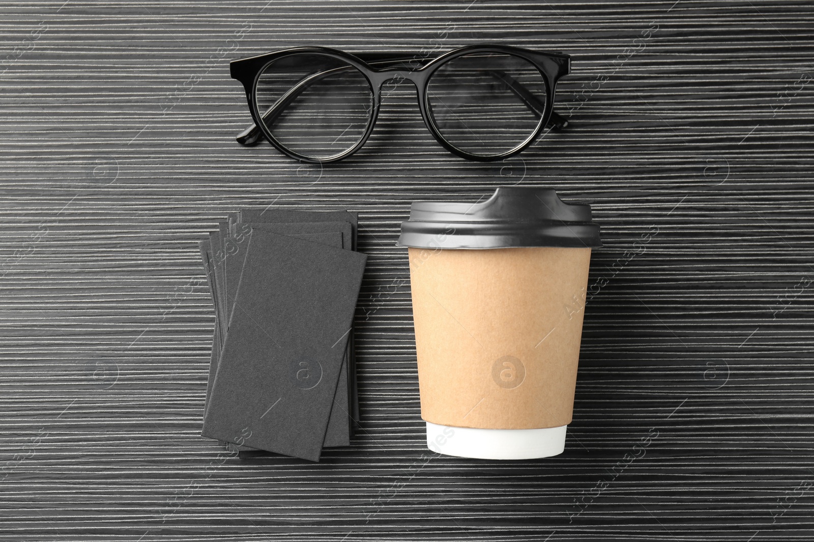 Photo of Blank black business cards, paper cup of coffee and glasses on wooden table, flat lay. Mockup for design