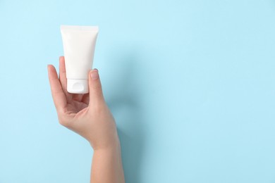 Woman with tube of hand cream on light blue background, top view. Space for text