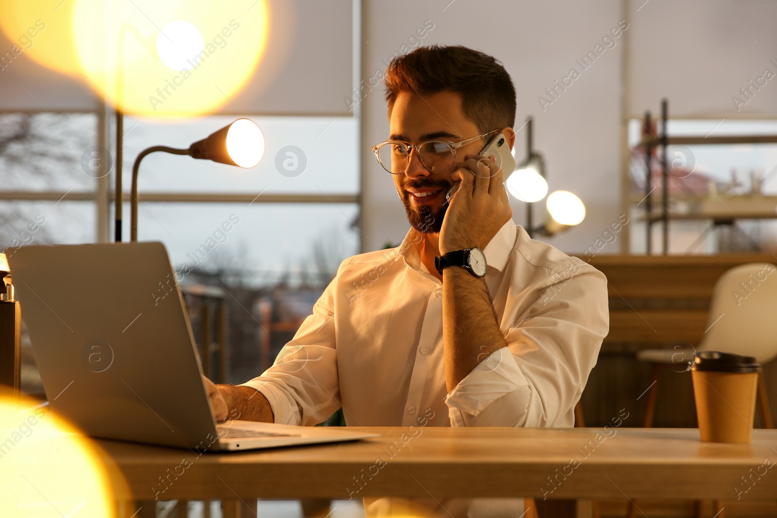 Photo of Man talking on smartphone while working with laptop in office