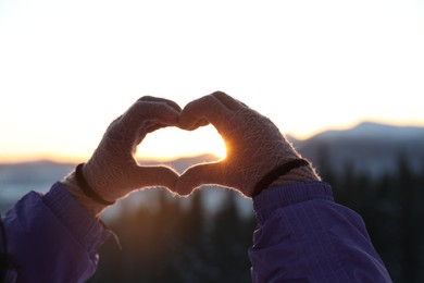 Photo of Woman making heart with her hands in mountains at sunset, closeup. Winter vacation