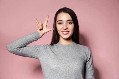 Photo of Woman showing I LOVE YOU gesture in sign language on color background