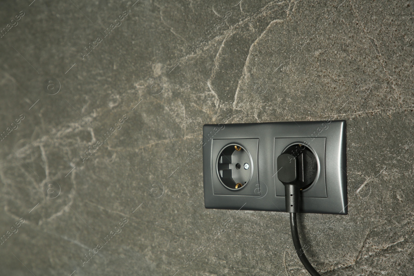 Photo of Power sockets with inserted plug on dark grey wall, space for text. Electrical supply