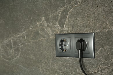 Photo of Power sockets with inserted plug on dark grey wall, space for text. Electrical supply