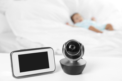 Photo of Baby monitor and camera on table near bed with child in room. Video nanny