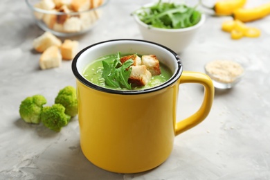 Photo of Metal mug of broccoli cream soup with croutons served on grey table