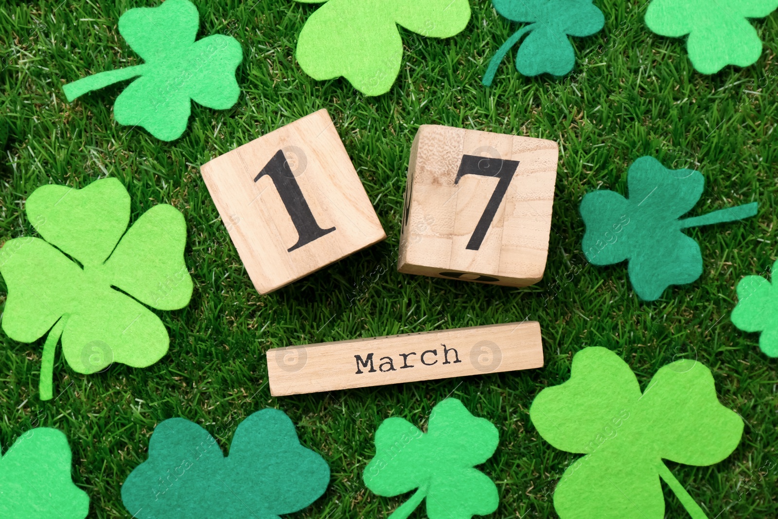 Photo of St. Patrick's day - 17th of March. Wooden block calendar and felt clover leaves on green grass, flat lay