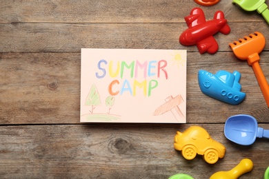 Card with text SUMMER CAMP, drawings and different sand molds on wooden table, flat lay