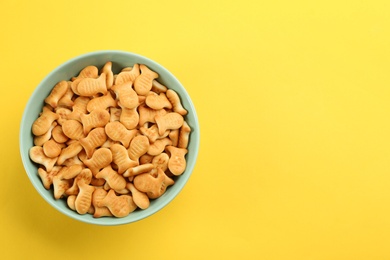 Delicious goldfish crackers in bowl on yellow background, top view. Space for text