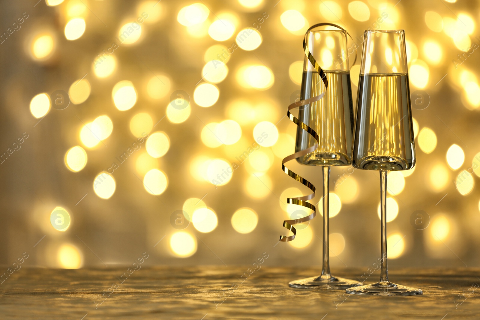 Photo of Glasses of champagne on table against blurred lights. Space for text