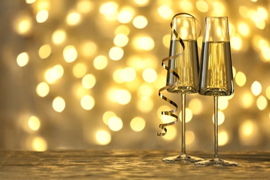 Photo of Glasses of champagne on table against blurred lights. Space for text