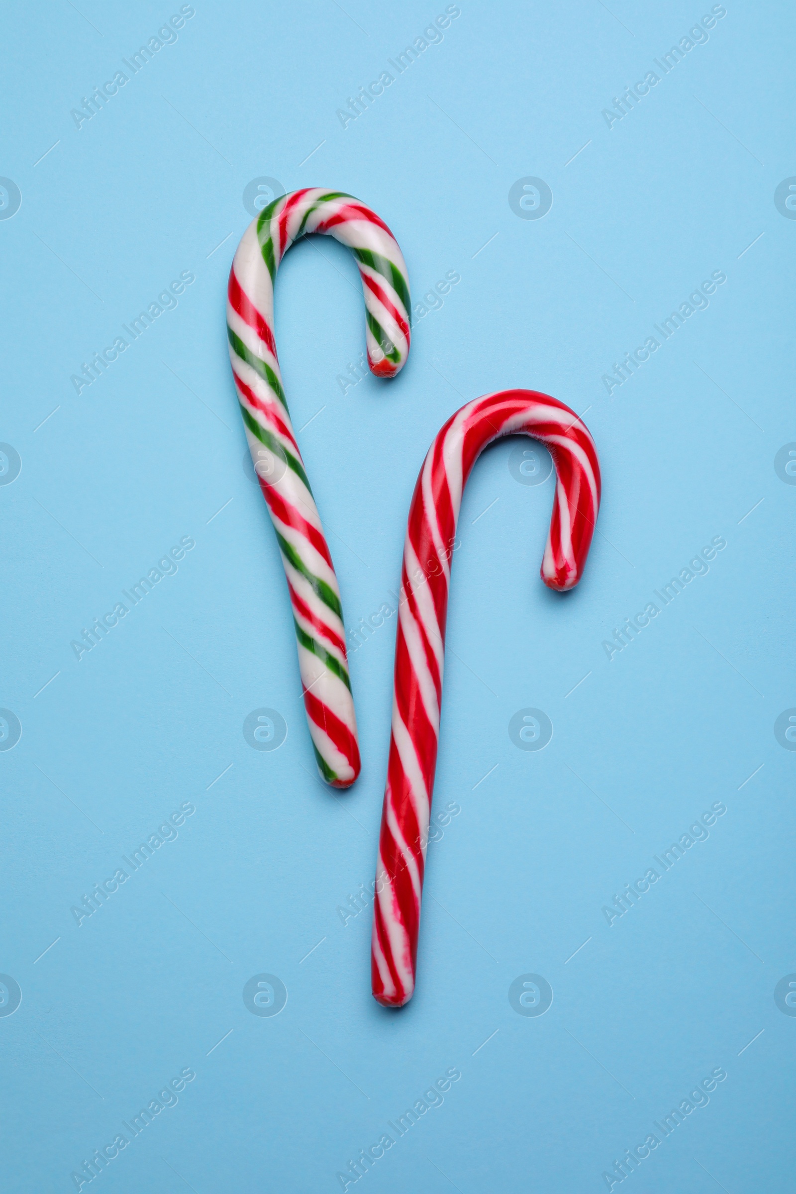 Photo of Two sweet Christmas candy canes on light blue background, flat lay