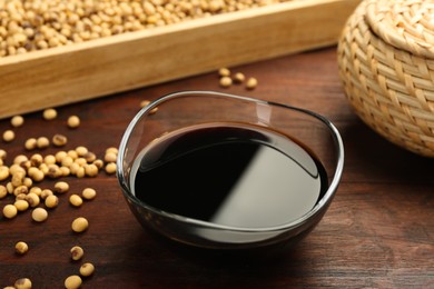 Photo of Soy sauce in bowl and soybeans on wooden table