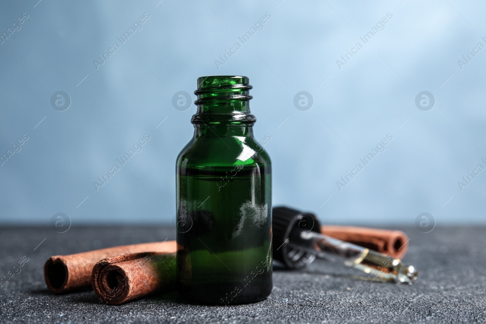 Photo of Bottle of essential oil and cinnamon sticks on table against blue background