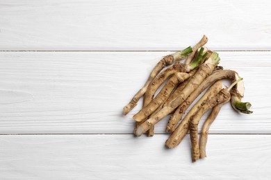 Cut horseradish roots on white wooden table, flat lay. Space for text