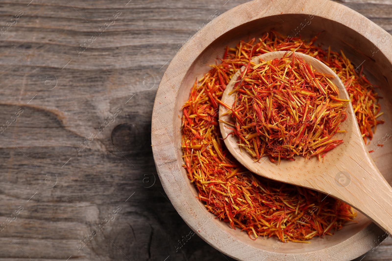 Photo of Aromatic saffron in bowl and spoon on wooden table, top view. Space for text