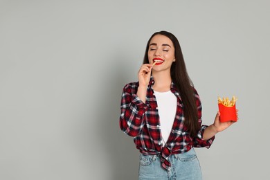 Photo of Beautiful young woman eating French fries on grey background. Space for text