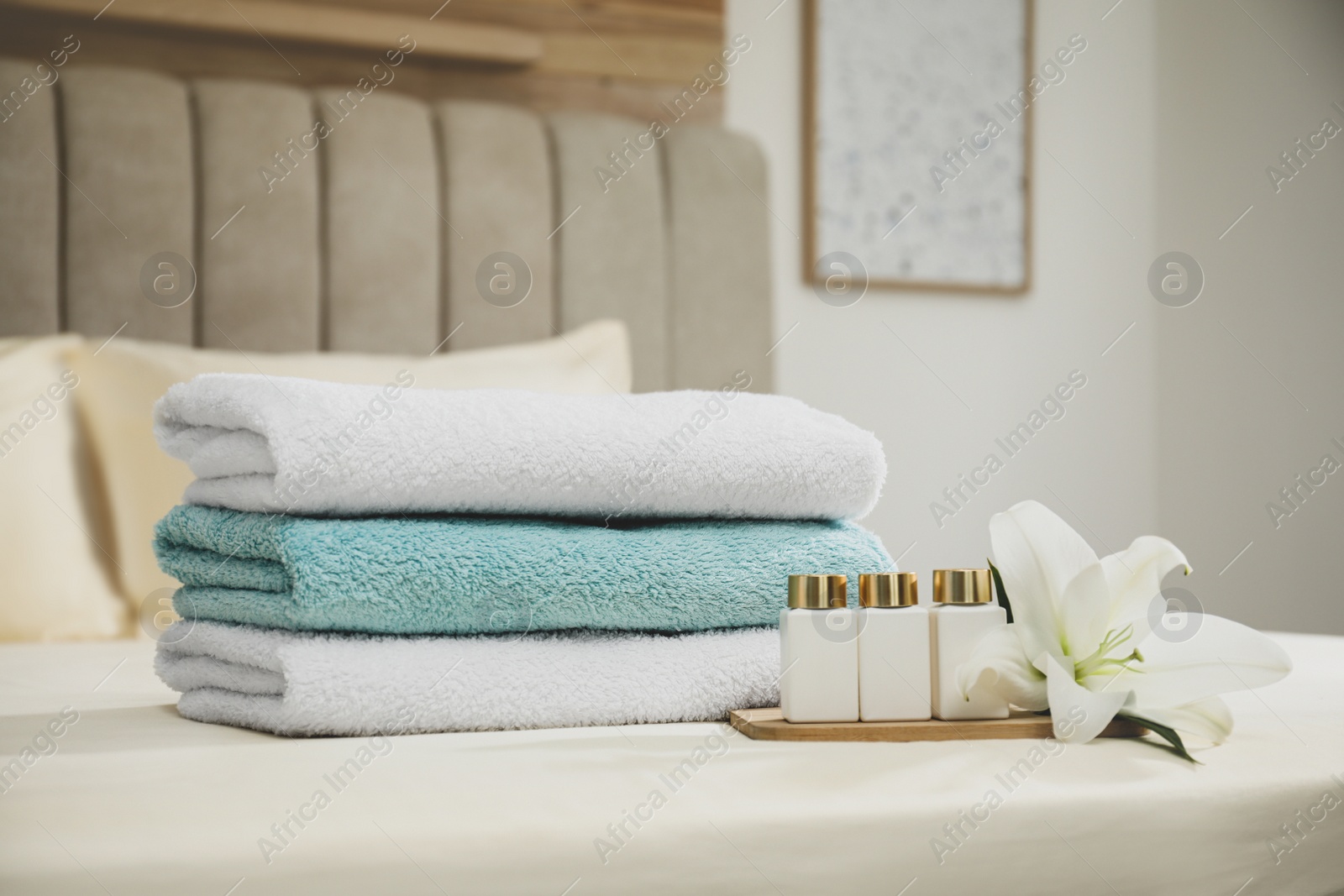 Photo of Stack of clean towels, flower and shampoo bottles on bed indoors