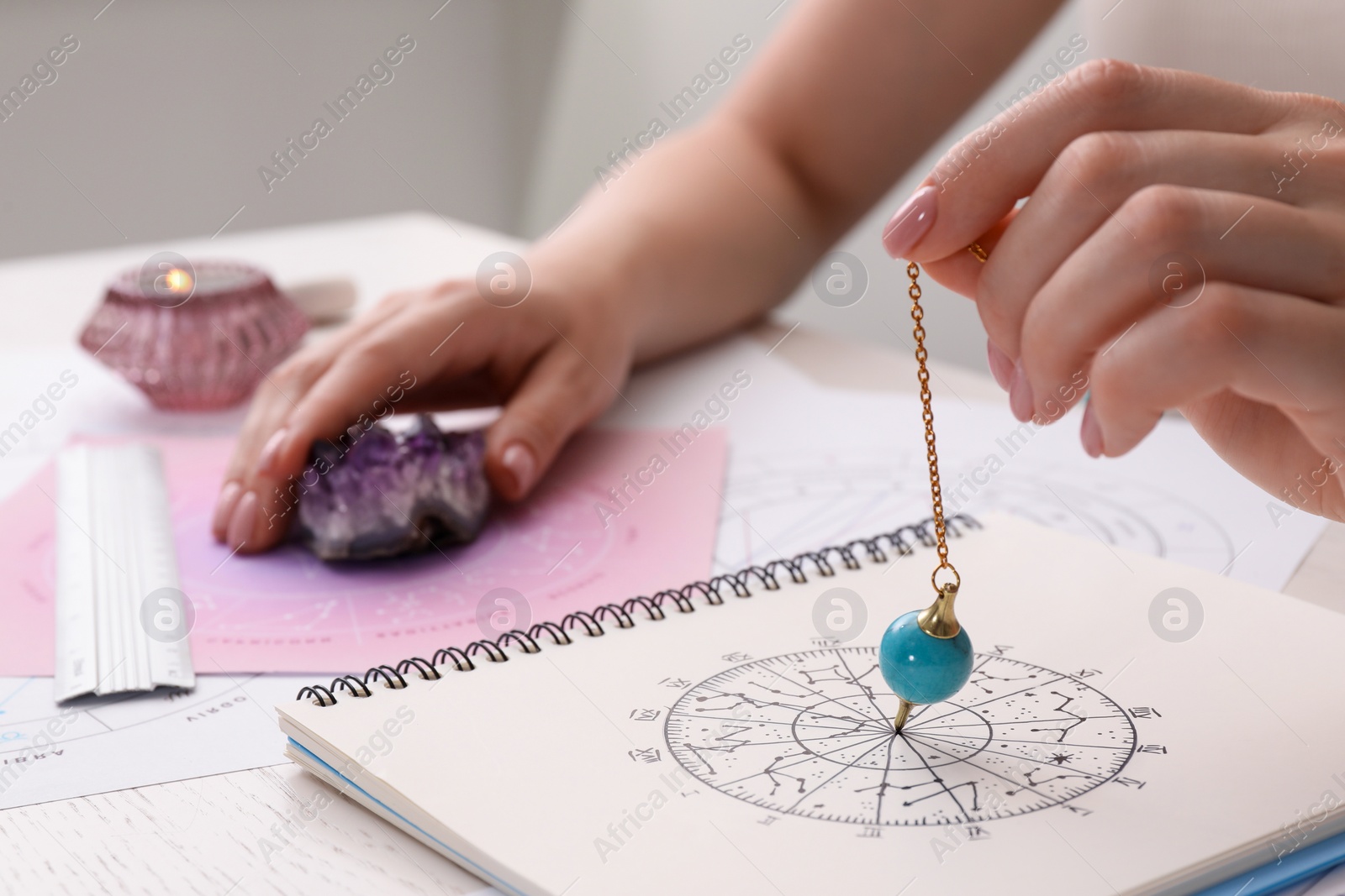 Photo of Astrologer using zodiac wheel and pendulum for fate forecast at table, closeup. Fortune telling