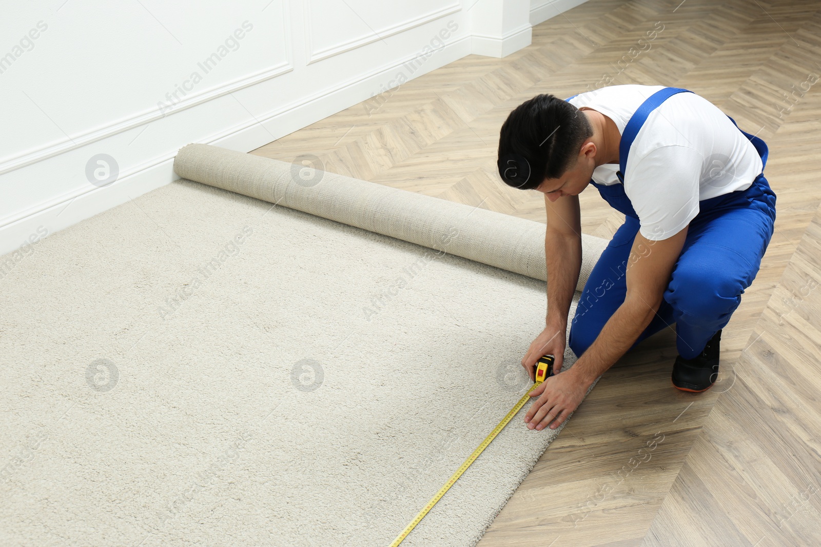 Photo of Worker with measuring tape installing new carpet indoors