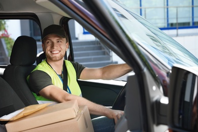 Young courier with parcels in delivery car