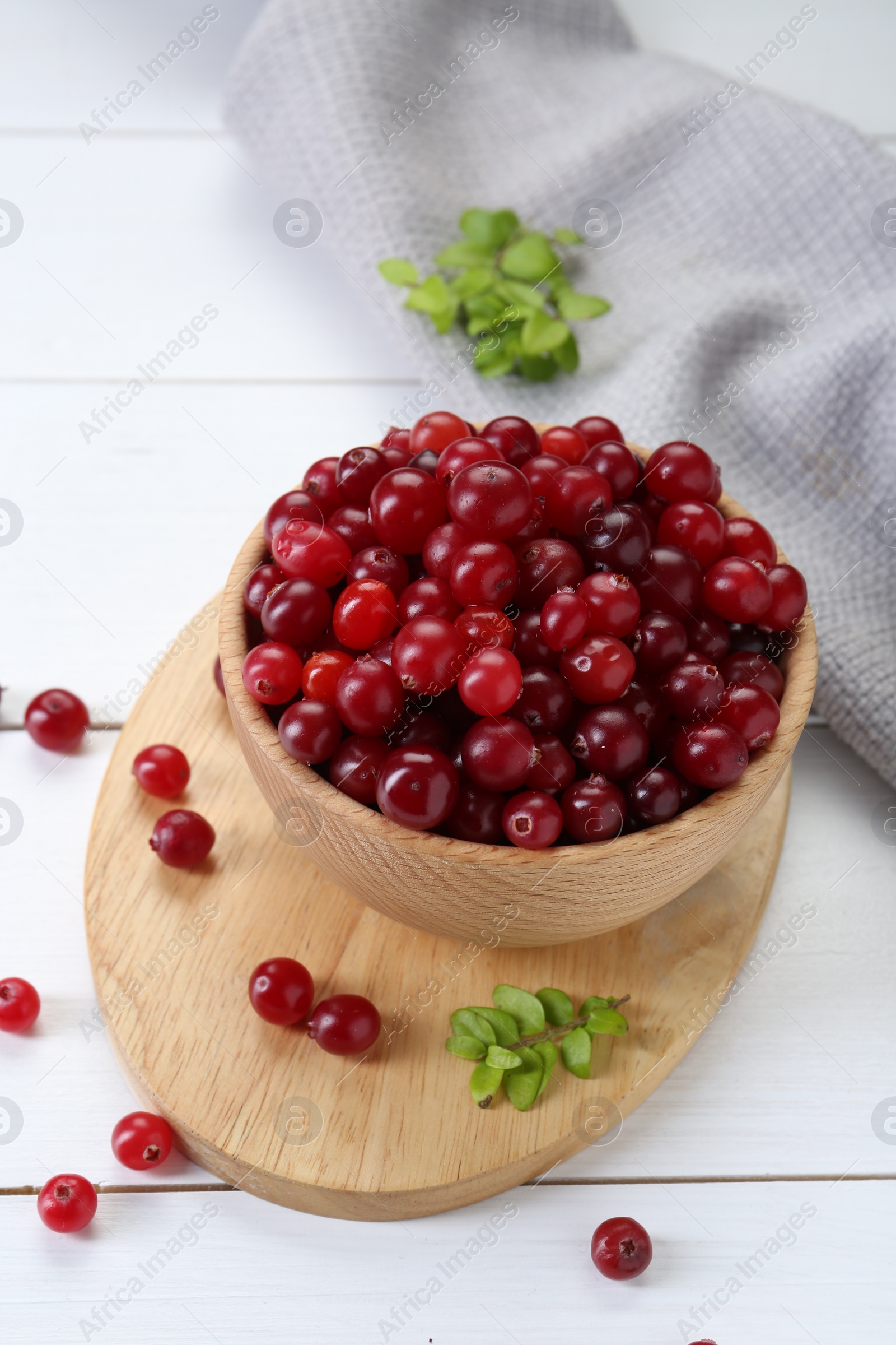 Photo of Fresh ripe cranberries in bowl and branches on white wooden table