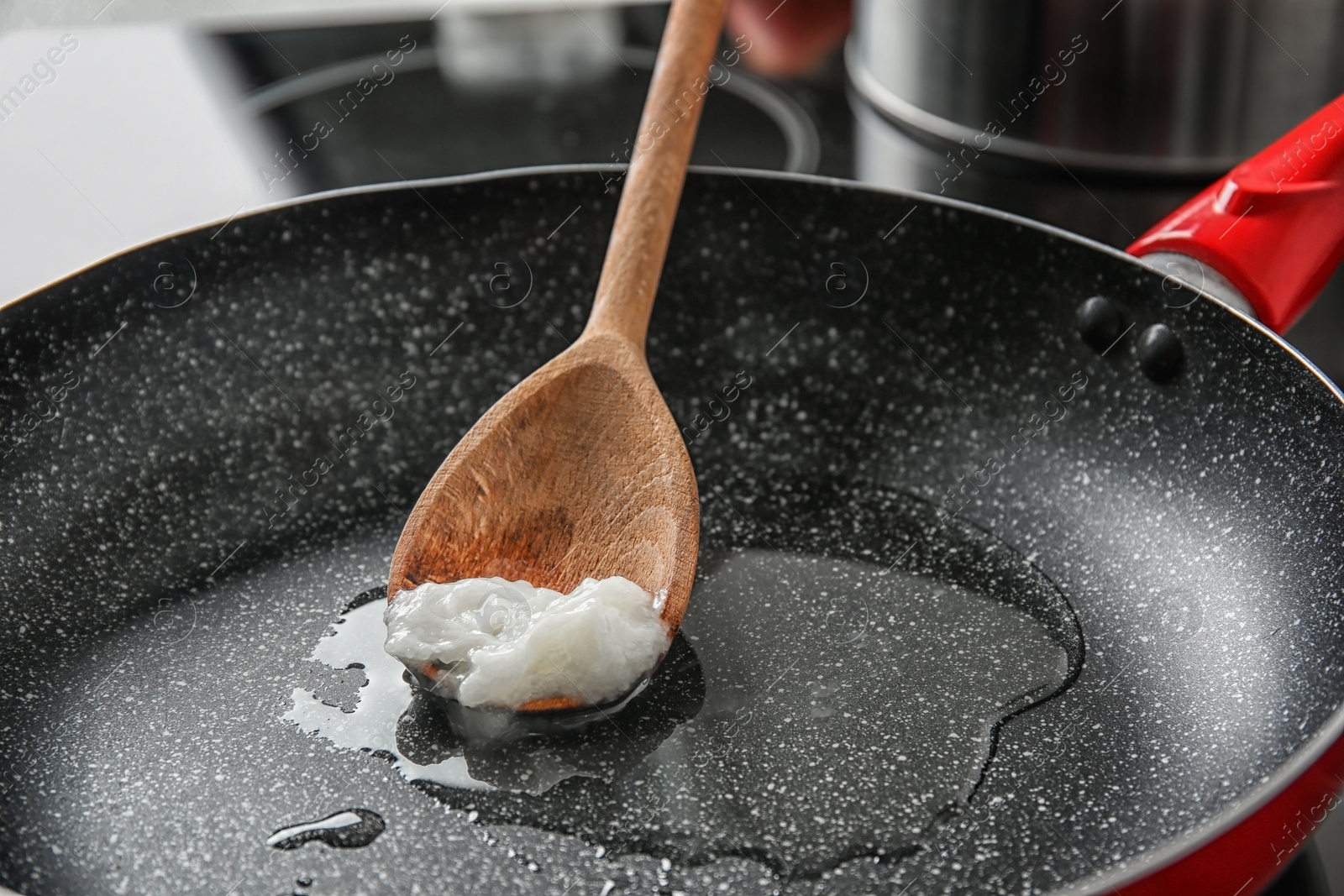 Photo of Wooden spoon with coconut oil in frying pan. Healthy cooking