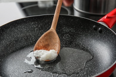 Wooden spoon with coconut oil in frying pan. Healthy cooking