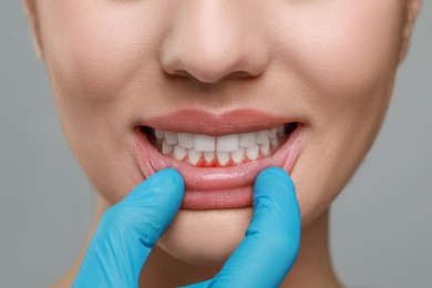 Image of Doctor examining woman's inflamed gum on grey background, closeup