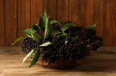 Photo of Ripe elderberries with green leaves in wicker basket on wooden table