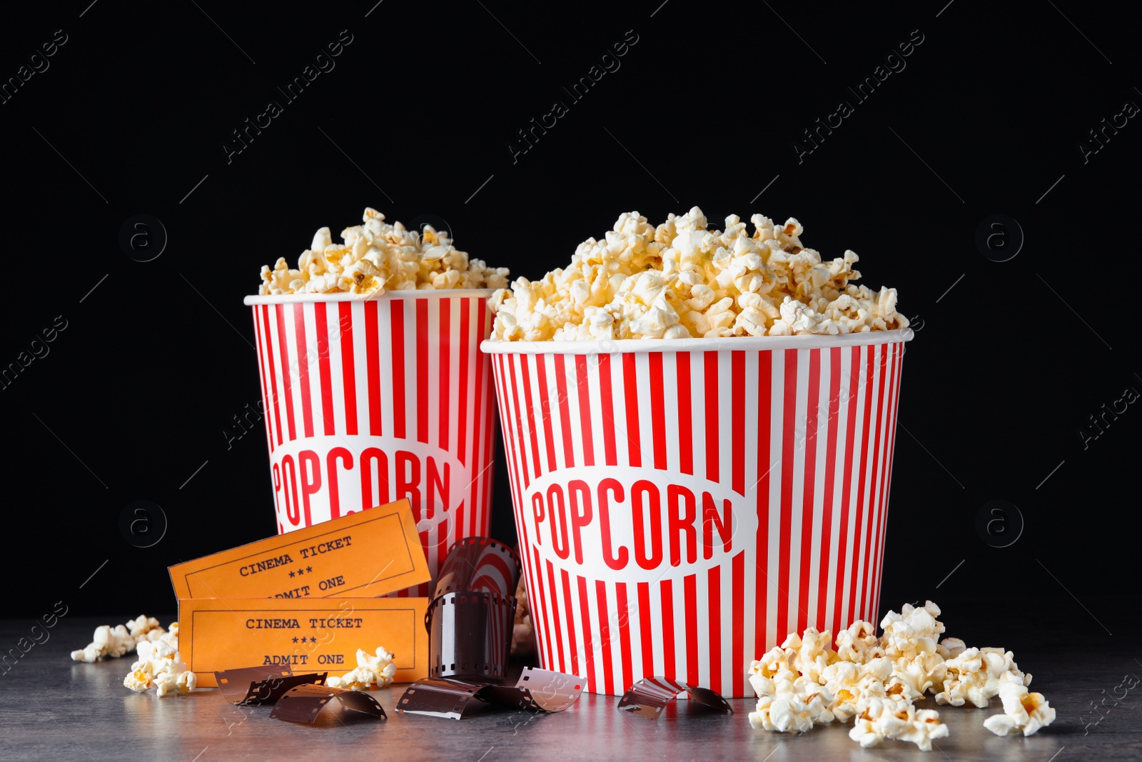 Photo of Popcorn, tickets and film footage on grey table against black background. Cinema snack