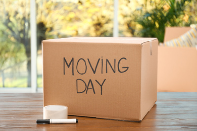 Photo of Cardboard box with words MOVING DAY and packaging items on wooden table
