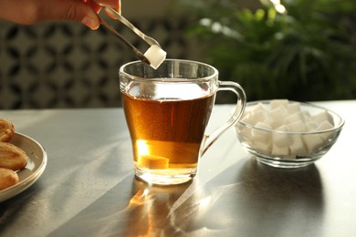 Woman adding sugar cube into cup of tea at dark table, closeup