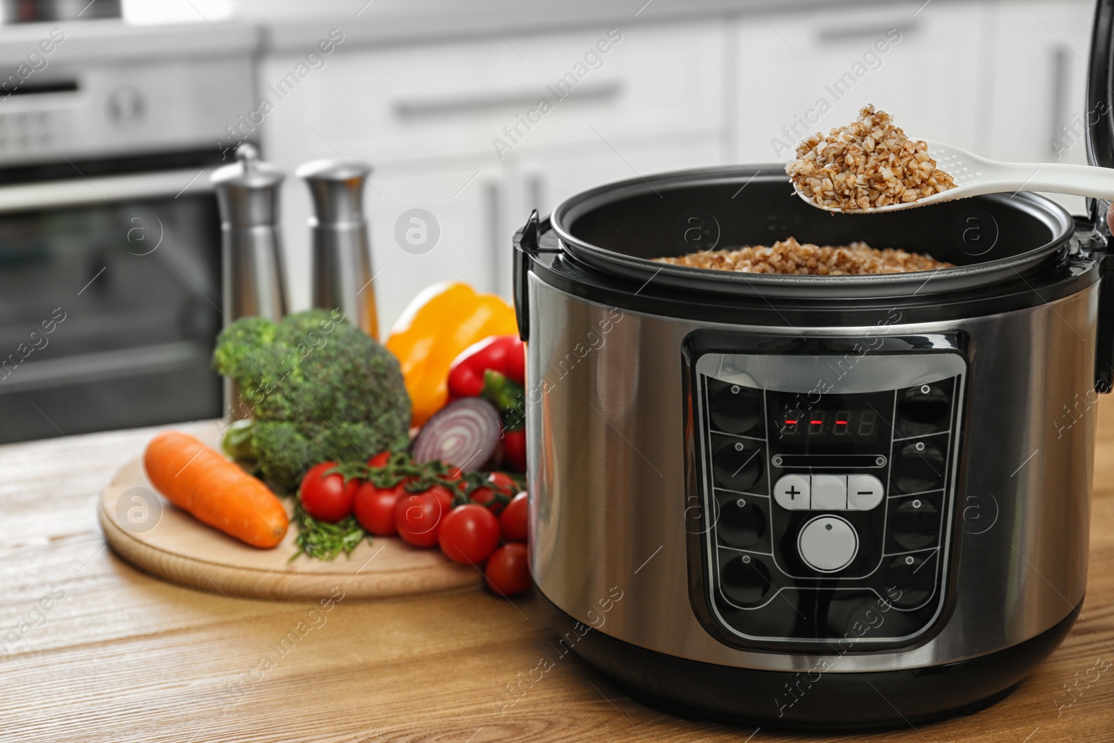 Photo of Spoon with delicious buckwheat over multi cooker near vegetables on table in kitchen. Space for text