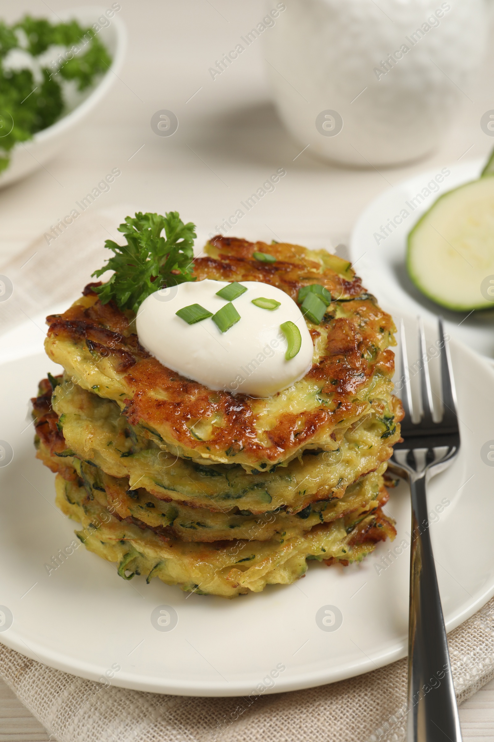 Photo of Delicious zucchini fritters with sour cream served on table, closeup